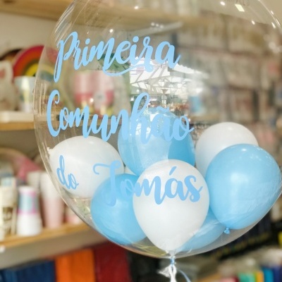 Balão transparente com balões azuis e brancos e texto comemorativo em azul, em loja com artigos coloridos