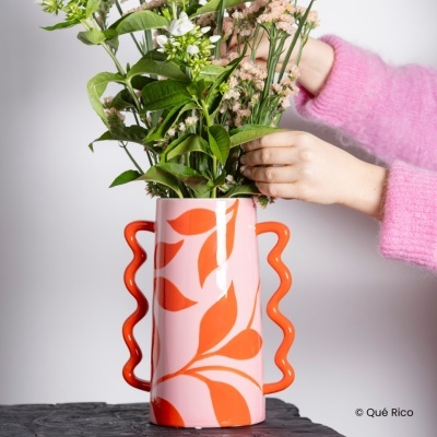 Jarro de cerâmica rosa e laranja com flores e folhas verdes