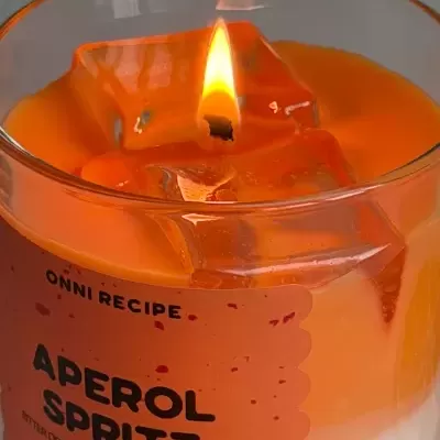 Vela aromática laranja e branca em copo de vidro com etiqueta Aperol Spritz.