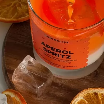 Vela aromática Aperol Spritz em vidro com base de madeira e fatias secas de laranja