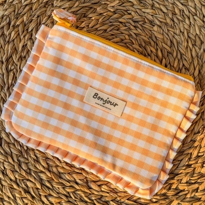 Estojo laranja e branco às quadrículas com fecho amarelo sobre superfície trançada de palha.