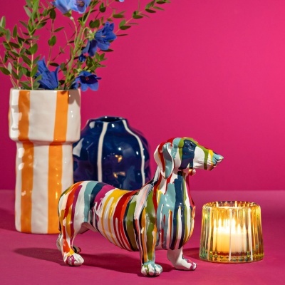 Escultura de cão colorida, vasos cerâmicos e vela em fundo rosa