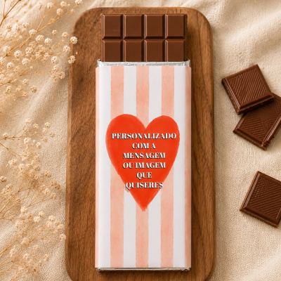 Barra de chocolate com embalagem personalizada com coração vermelho e texto, sobre base de madeira com flores secas.