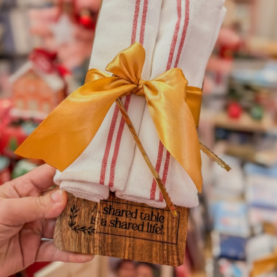 Conjunto de panos de cozinha brancos com riscas vermelhas amarrados por fita dourada com suporte de madeira com texto gravado