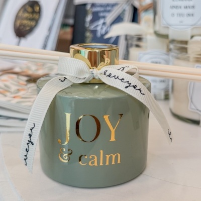 Difusor de ambiente verde-cinzento com laço branco e texto dourado JOY & calm