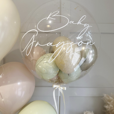 Balão transparente com balões e glitter dentro, texto Baby Grayson, com balões pastel ao redor
