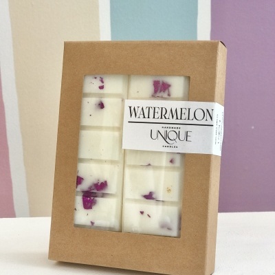 Caixa de vela artesanal branca com pedaços roxos e etiqueta Watermelon sobre fundo colorido