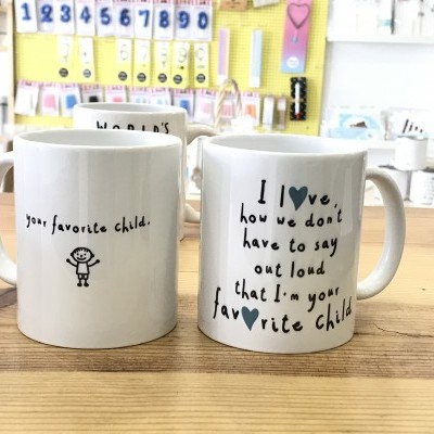 Dois canecos brancos com texto preto e desenhos colocados sobre uma mesa de madeira