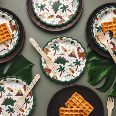Pratos decorativos com padrão de dinossauros e waffles dourados sobre superfície cinzentas e folhas verdes