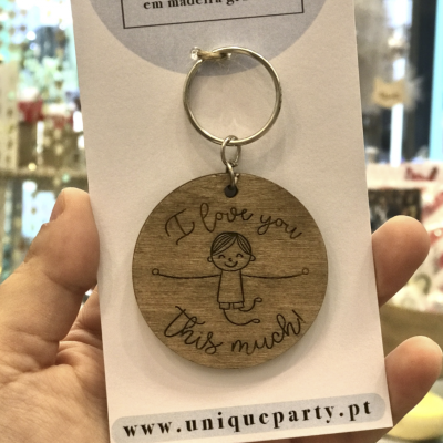 Porta-chaves redondo em madeira gravada com texto e imagem de criança, pendurado em cartão branco com textos relacionados.