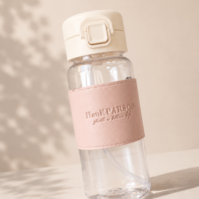 Garrafa transparente com tampa creme e proteção rosa com texto HanKPARSON