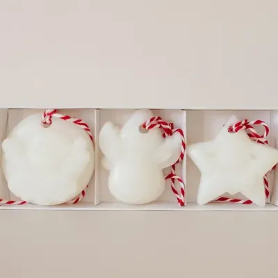Três decorações brancas de Natal com cordão vermelho e branco em caixa branca.