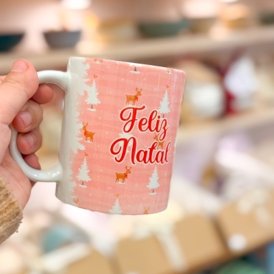 Caneca branca decorada com pinheiros e renas com texto Feliz Natal