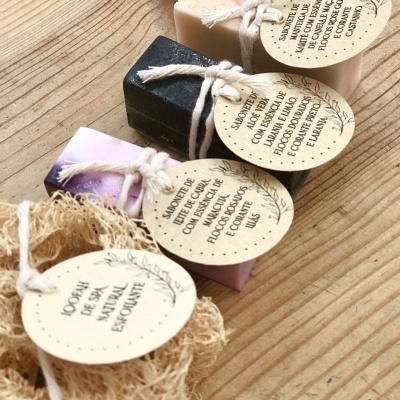 Conjunto de quatro sabonetes artesanais com etiquetas em papel reciclado pendurados por cordão branco sobre madeira clara