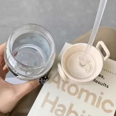 Frasco transparente com tampa branca e canudo sobre livro