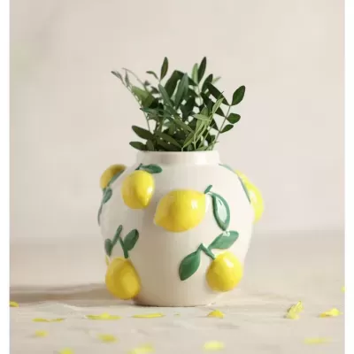 Vaso branco com limões em relevo e folhas verdes com ramos dentro