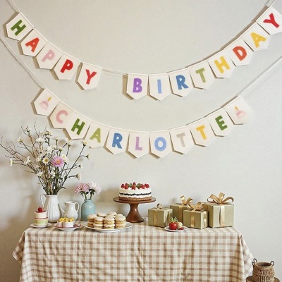 Decoração de festa de aniversário com faixa colorida, mesa com bolo, presentes e flores.