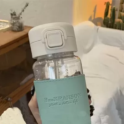 Garrafa transparente com tampa branca e capa azul claro com texto em ambiente interior