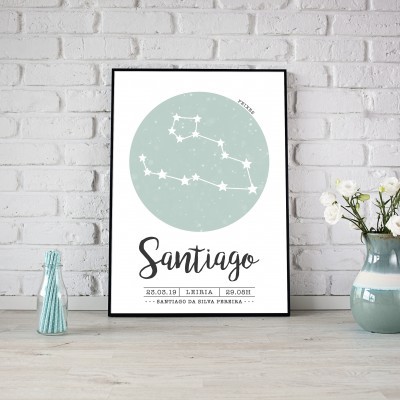 Quadro decorativo com padrão do signo Touro e texto Santiago na moldura preta sobre mesa com garrafa azul e jarro com flores