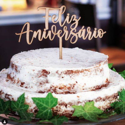 Bolo de aniversário branco decorado com folhas verdes e topo de bolo 'Feliz Aniversário'