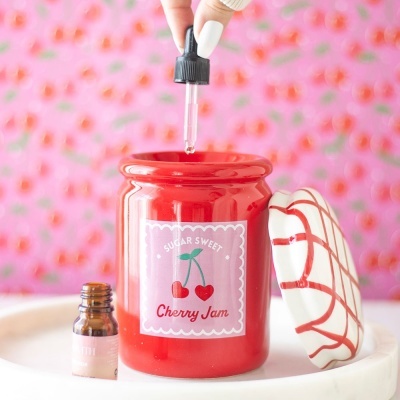 Frasco vermelho cerâmico de geleia de cereja com tampa, pipeta e fundo rosa com cerejas