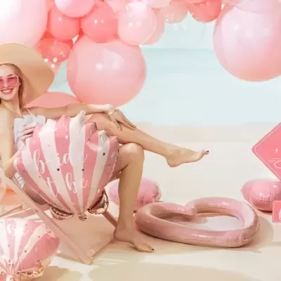 Mulher com chapéu e óculos rosa numa espreguiçadeira rosa com balões e decoração cor-de-rosa