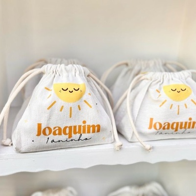 sacos de tecido branco com sol amarelo e texto Joaquim 1 aninho