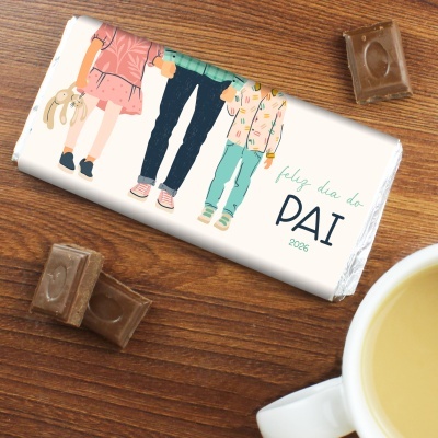 Chocolate com embalagem ilustrada para o Dia do Pai em cima de mesa de madeira com pedaços de chocolate e uma chávena de chá.