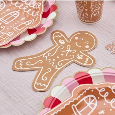 Guardanapo em forma de biscoito de gengibre com decoração branca e pratos de papel coloridos num fundo de tecido claro.