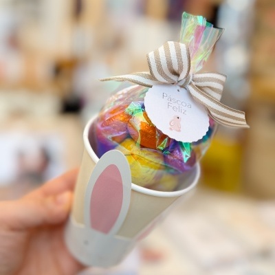 Copo decorado com orelhas de coelho segurando doces embrulhados em celofane.