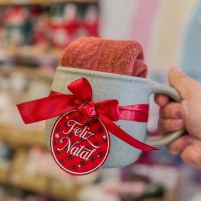 Caneca cinzenta com fita vermelha e selo 'Feliz Natal' com pano vermelho dentro