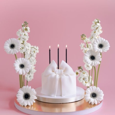 Bolo branco com velas e flores decorativas num fundo rosa