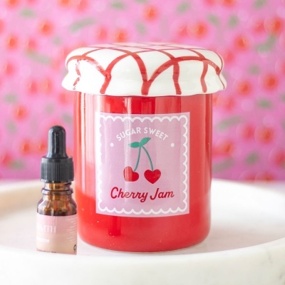 Frasco decorativo de geleia de cereja e pequeno frasco com conta-gotas em fundo rosa com padrão de cerejas