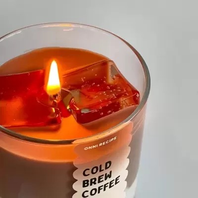 Vela aromática Cold Brew Coffee em copo de vidro com cera castanha e branca e cubos vermelhos decorativos