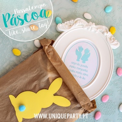 Saco castanho aberto, quadro branco decorativo com texto e dois passarinhos azuis, recorte de coelho amarelo com pompom azul, confeites coloridos espalhados