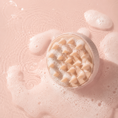 Escova redonda rosa com cerdas em espuma branca sobre fundo líquido rosa