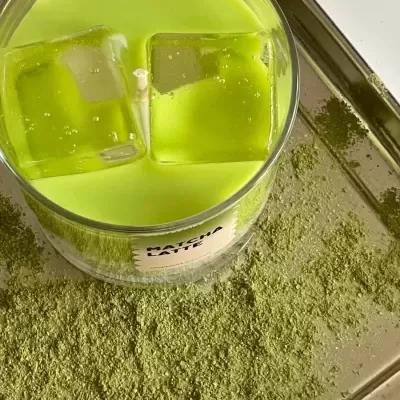 Vela verde em copo de vidro com rótulo MATCHA LATTE e pó verde espalhado