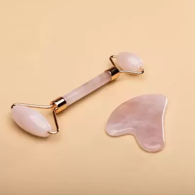 Ferramentas de massagem facial em quartzo rosa sobre fundo bege