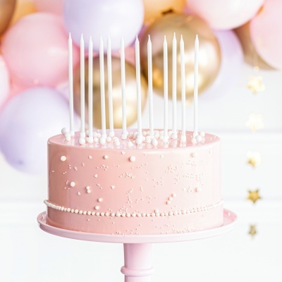 Bolo rosa claro decorado com pequenas pérolas e 12 velas brancas em suporte rosa e balões ao fundo