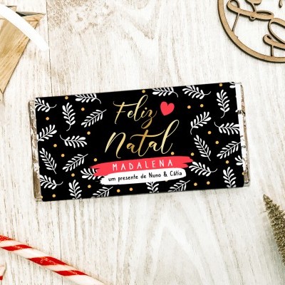 Barra de chocolate com design natalício e texto em português sobre superfície de madeira clara