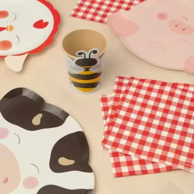 Pratos infantis em forma de galinha, porco e vaca, copo com abelha, guardanapos xadrez vermelho e branco