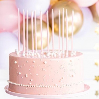 Bolo rosa com velas longas e pérolas brancas sobre suporte cor-de-rosa em fundo festivo