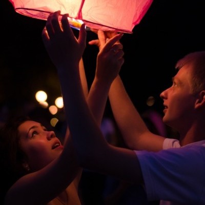 Pessoas segurando uma lâmpada voadora de papel cor-de-rosa iluminada durante a noite