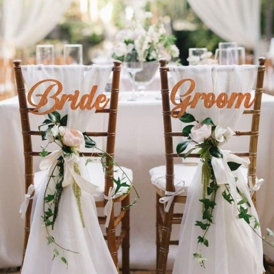 Cadeiras decoradas com tecidos, flores e sinais Bride e Groom
