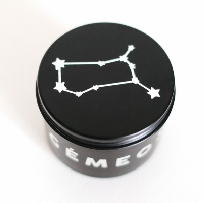 Frasco preto com tampa decorada com constelação branca e texto parcial CÉMEO