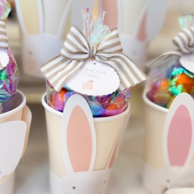 Copo decorativo com orelhas de coelho e bombons embrulhados coloridos com laço e etiqueta de Páscoa