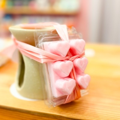 Queimador de cerâmica verde com corações rosa amarrados com fita cor-de-rosa numa mesa de madeira.