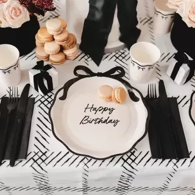 Mesa decorada para aniversário com pratos brancos e pretos, macarons, rosas e copos com laços pretos
