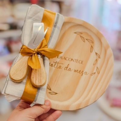 Prato redondo de madeira com gravação, guardanapo bege com riscas, fita mostarda e talheres de madeira