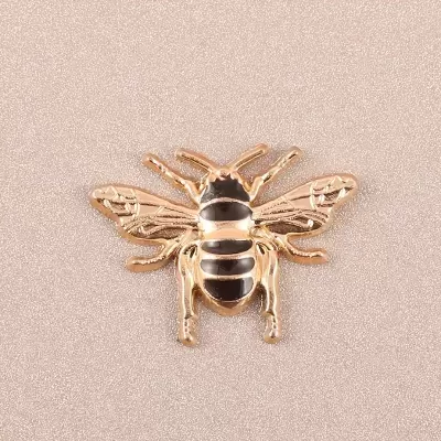 Broche dourado e preto em forma de abelha sobre fundo rosa claro texturizado